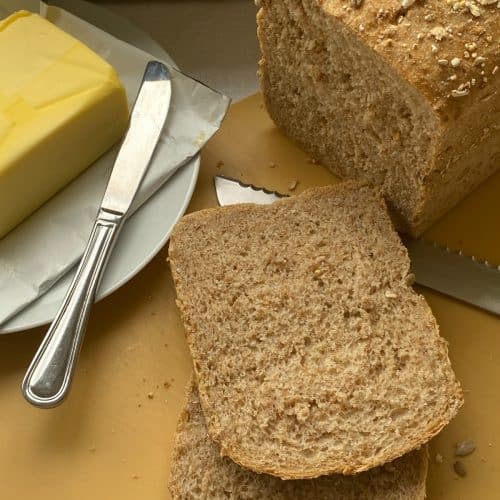 Sliced ancient grain bread with plate of butter and knife in the background.