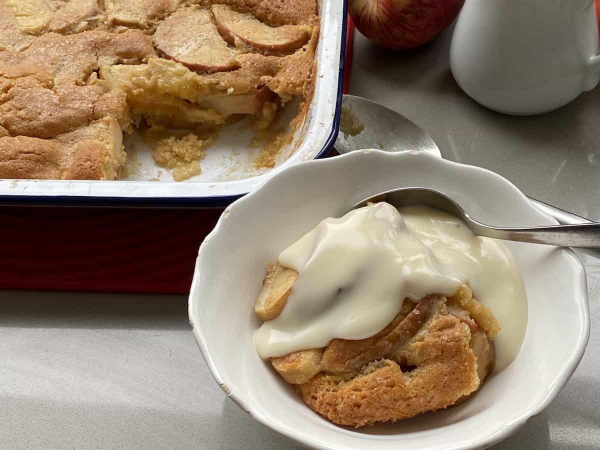 Portion of Apple Sponge Pudding with custard in a white dish.