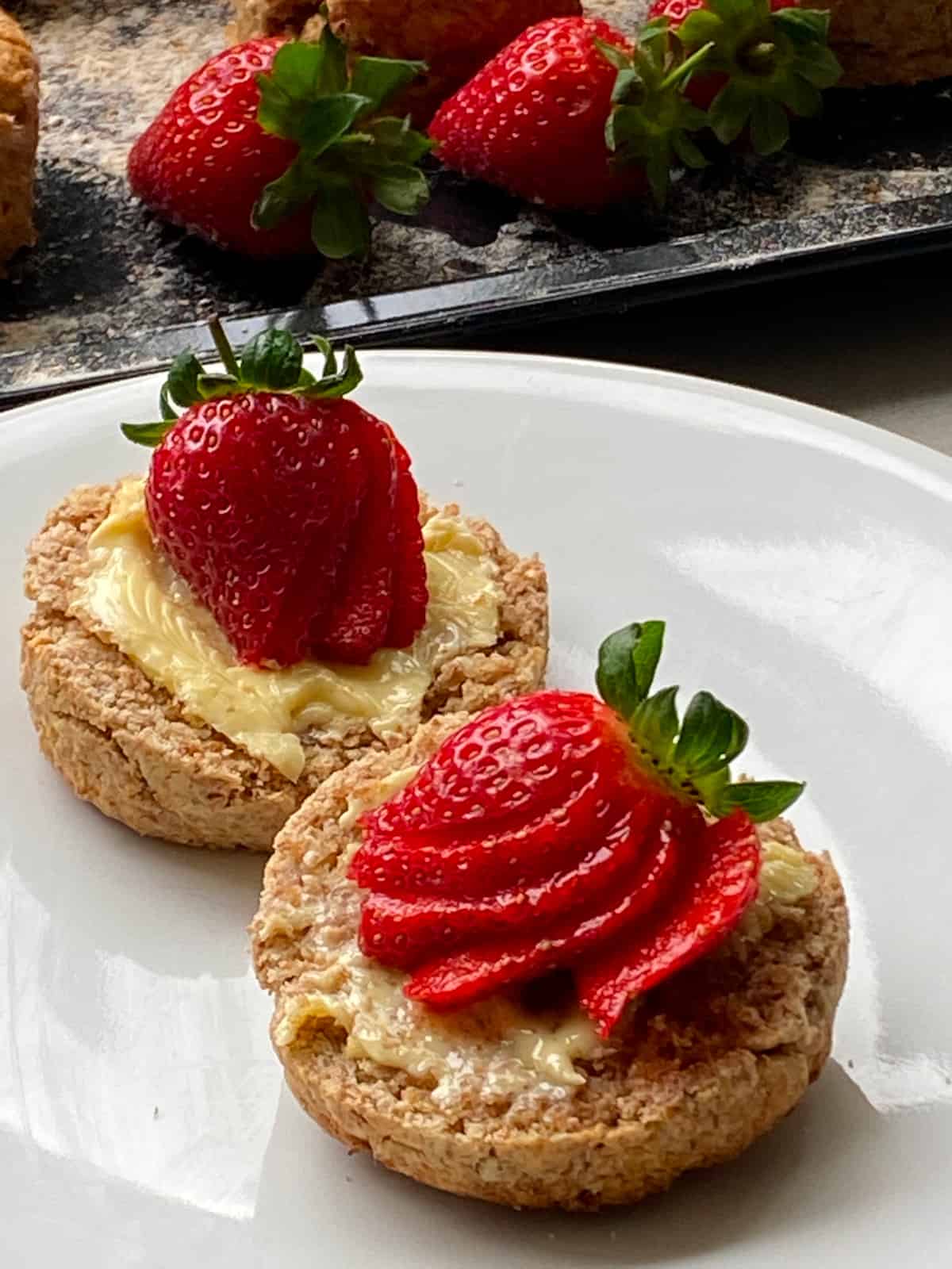 Sliced scone on a white plate, with butter and slices of strawberries on the top.