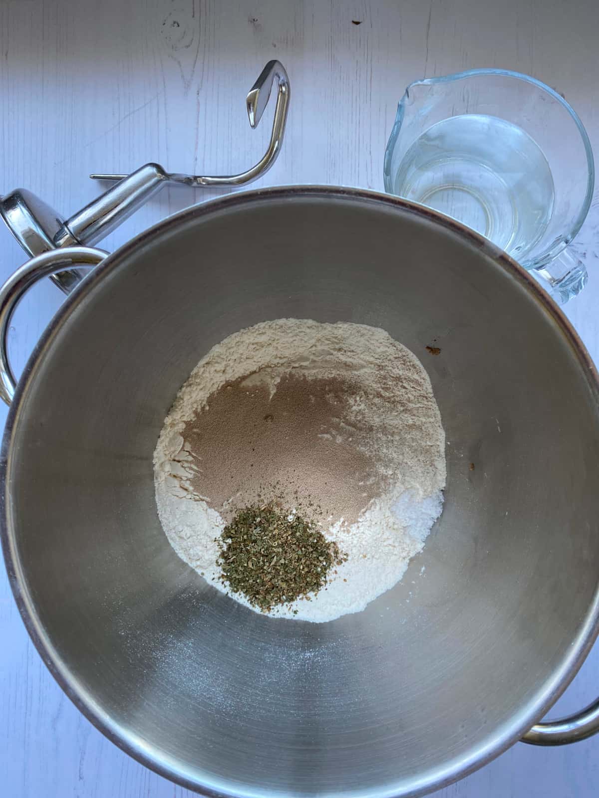 Dry Ingredients in a bowl, with a jug of water and a dough hook on the side.