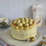 Red Velvet Cake on a cake stand decorated with white chocolate truffles and freeze dried raspberries.