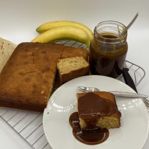 Banana Sponge pudding with a slice served on a white plate and a jar of toffee sauce.