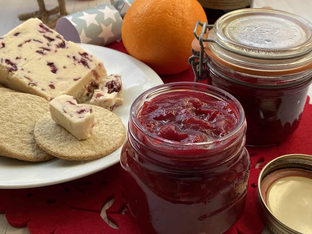 Platter of cheese and crackers with jars of cranberry sauce.