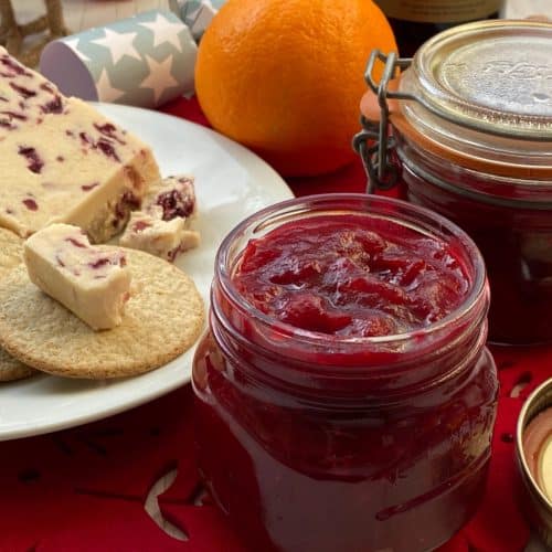 Jar of cranberry sauce with a plate of cheese and crackers on the side.
