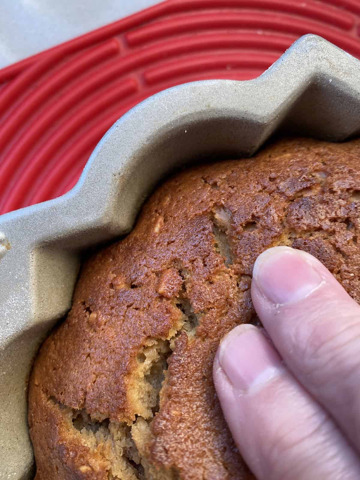 Fingers pulling baked sponge from the inside edge of a bundt pan. 