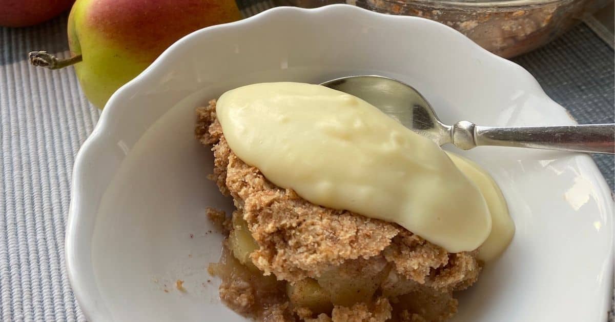 Portion of Apple Crumble with custard in a white dish. 