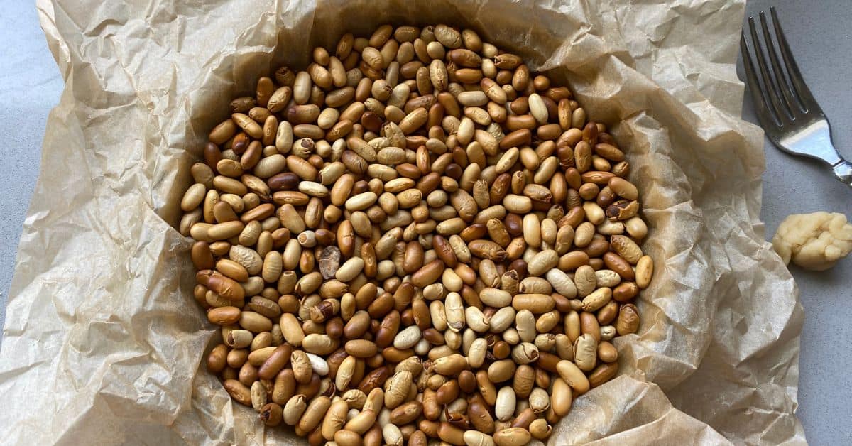 Pastry case lined with baking parchment and filled with dried beans.